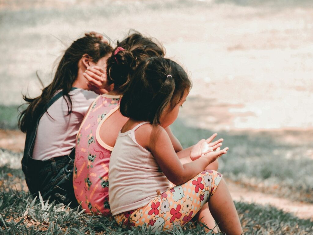 Drei Kinder sitzen auf einer Wiese. Eins betrachtet seine Hände.